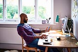 Man looks at his phone while sitting at his desk.