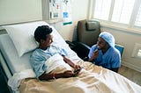 A smiling nurse jokes with a boy patient in a hospital bed.