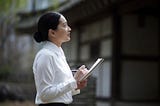 Asian businesswoman taking notes outside while looking at a building.