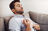 A young man holding his chest in pain while relaxing on a sofa at home.