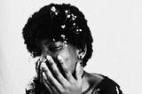 Black & white image of a woman holding her face in her hands. She might be laughing or crying.