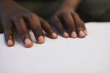 A closeup photo of a black person’s hands reading Braille.