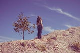 A photo of a woman standing on top of a dune and looking away to the sky