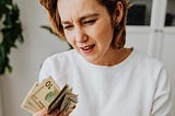 Woman holding money from an envelope and looking disappointed.