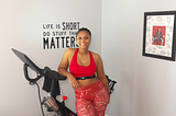 A photo of Teresia Greer and her Peloton bike in her living room. “Life is short, do stuff that matters” is on her wall.