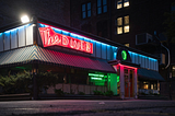 A diner at night, reflections in the puddles after a storm