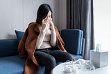 A woman sneezes into a tissue and wipes her nose.