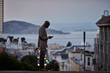 Black businessman checking phone while on the street in San Francisco in the evening.