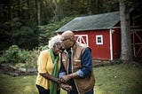 A photo of an elderly black couple in front of a barn-looking structure in a rural area.