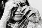 A black-and-white photo of an Indian bride crying, her hands wiping her tears.