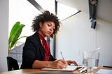 Confident Black woman writing down invoice at her computer.