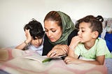 A photo of a Muslim mother reading a book to her two young boys.