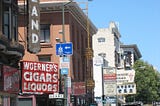Woerner’s Cigars and Liquors in the foreground and other SF shops along the street.
