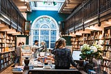 Inside a bookstore with balconies and a large stained glass window. Customers look around.