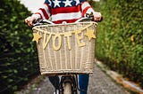 Person riding bicycle with “VOTE” banner on it.