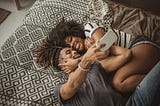 A photo of a happy couple taking a selfie while laying on a bed.