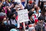 A protestor in a crowd holds up a sign that says “TRANS BLACK LIVES MATTER.”