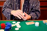 An elderly man playing poker in a bathrobe and a baseball cap, actively counting his chips.