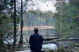 Man sitting on bench in front of lake surrounded by forest