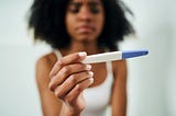 Black woman holding a pregnancy test with an upset expression.