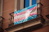 A photo of the trans flag hanging on a balcony.