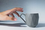 white tea a hand is reaching out for a grey tea mug on a white table with plain grey wall behind you can’t see inside the cup