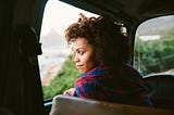 Black woman looking out the window of her car from the driver seat.