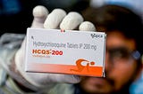 A pharmacist displays a box of hydroxychloroquine tablets.