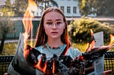 Teen girl holding burning newspaper with leaping flames.