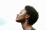 A photo of a black woman with her eyes closed, head tilted towards the sky, looking peaceful and serene.