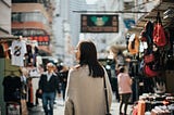 A photo of the back of a young Asian woman walking through a local market street in Hong Kong.