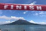 Banner reading “Finish” above a smoking volcano in the distance and bay in the foreground.