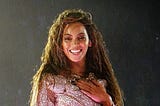 The singer Beyoncé smiling on stage in a white sequin-covered leotard.