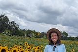 Ron Rivers standing in a sunflower farm and wearing a sun hat, sky blue colour half sleeves shirt and sea green shirts with a wide smile on his face looking at you.