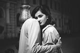 A Monochrome photo of a woman looking at the camera while a person is hugging her.