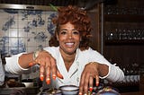 A photo of Kelis in the kitchen, hovering over a plate of appetizers.