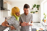 A couple in their kitchen looking at one of their phones.