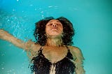 A person floating in a pool with their right arm outstretched.
