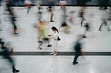An overhead photo of an Asian woman standing still as blurred people walk by her.