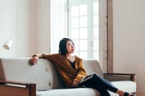 Asian woman sitting on her sofa looking out the frame.