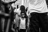 A black and white photo of a young Black boy wearing a face mask at a protest in LA.