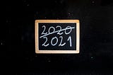 Black Board showing “(Bye) 2020, (hello) 2021” written on it by white chalk.