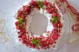 A wreath made of stiff sweet white vegan meringue sits on a plate and is decorated with red berries and leaves
