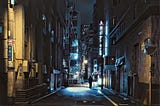 Dark empty city street at night, save for a lone dark figure.
