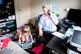 Mom works from home on the computer and phone while her daughter copies her and plays around her.