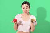 A woman thinks about the choice to either eat an apple or a cake