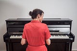 Rear view of a woman in a red dress playing the piano.