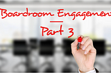 A hand holding a red pen writing on the screen the words “boardroom engagement — part 3” with a blurred picture of a boardroom in the background.