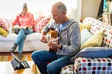 An older man learning guitar by watching an online tutorial on his tablet.