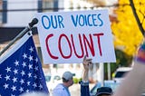 Protestor holding a sign that says “OUR VOICES COUNT.”